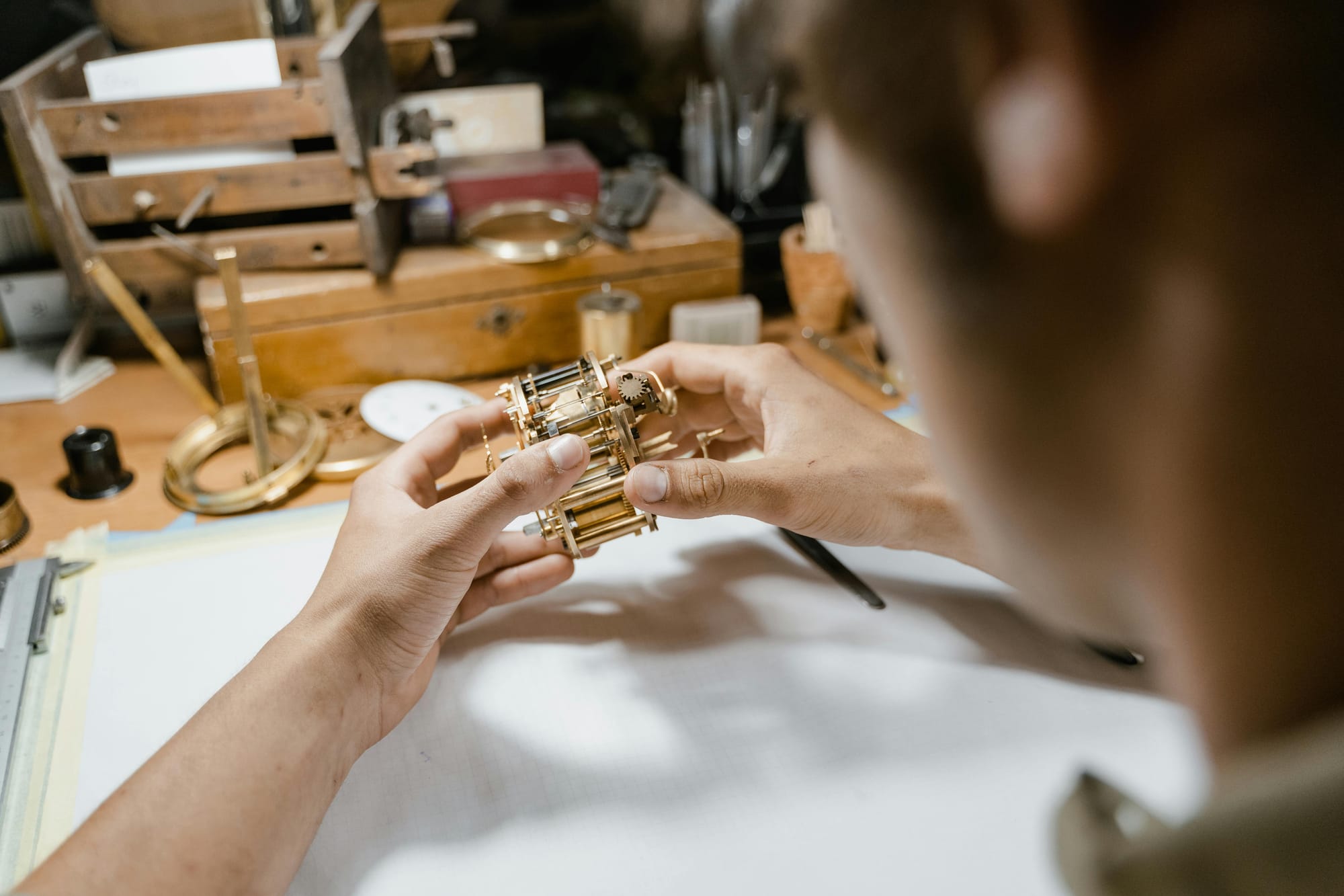 Overhead view of a watchmaker carefully handling a mechanism at an organized workbench full of tools